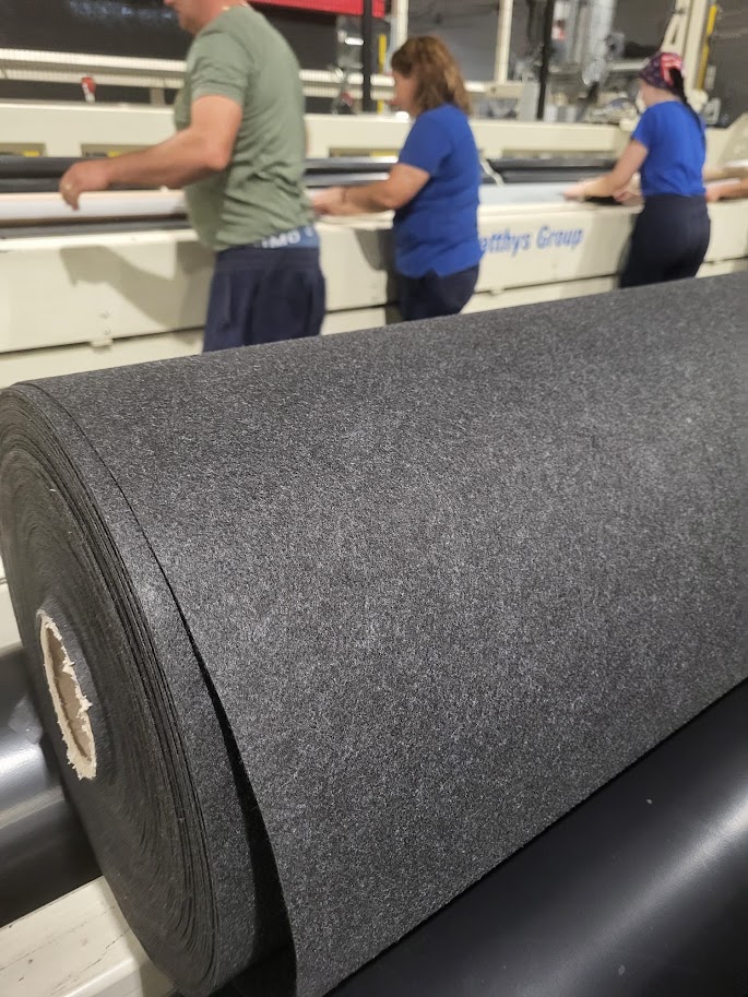 A roll of anthracite textile with workers and production equipment in the background